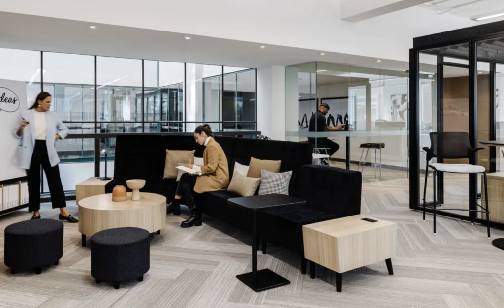 Modern office environment with black couch and tables. People engaging.