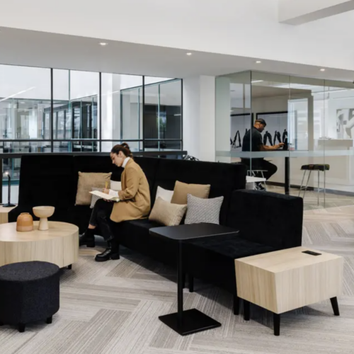 Modern office environment with black couch and tables. People engaging.